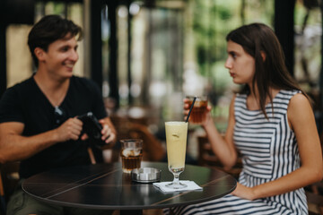 Two young friends are captured in a candid moment, enjoying cold beverages at a cozy outdoor cafe. The scene embodies friendship, relaxation, and leisure in a casual setting.