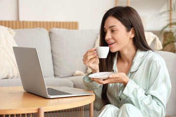 Young woman in green pajamas working with coffee and laptop on table at home