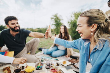 Group of friends having a joyful picnic in a park, sharing food and laughter. Two friends give each other a high five, capturing the essence of friendship and happiness.