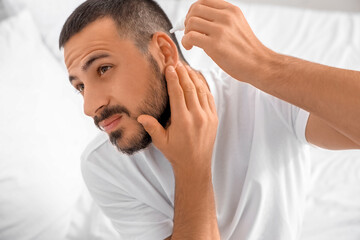 Young man with hearing problem putting drops in his ear at home, closeup