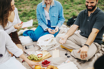 A group of multiracial friends enjoys a picnic in nature, sharing laughter and food on a cloudy...