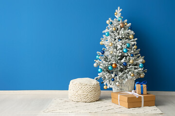 Beautiful Christmas tree in pot with gift boxes and ottoman near blue wall
