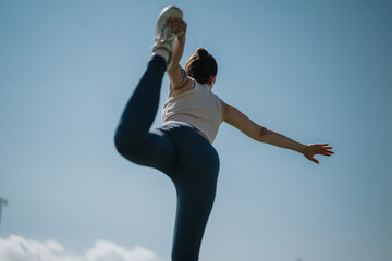 Obraz premium A woman performing a yoga pose outdoors, balancing gracefully under a clear blue sky. Her athletic form and tranquil environment embody fitness and mindfulness in nature.