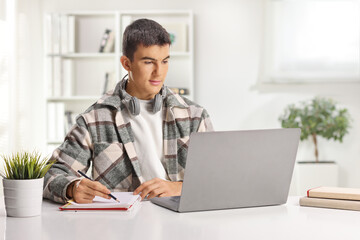 Student with headphones writing and browsing on a laptop computer at home