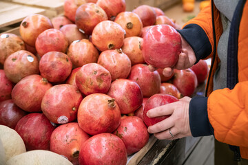 woman in a supermarket selects ripe pomegranates from a large assortment .