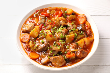 Delicious stew with vegetables in bowl on white wooden table, closeup