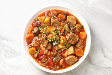 Delicious stew with vegetables in bowl on white marble table, top view