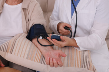 Doctor measuring patient's blood pressure indoors, closeup