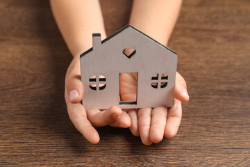 Adoption concept. Kid with cutout of house at wooden table, closeup
