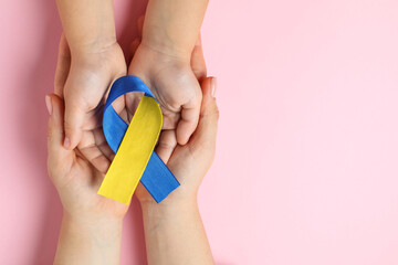 Woman with child holding yellow and blue ribbon on pink background, top view. Down syndrome awareness