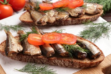 Delicious sandwiches with sprats, dill and tomato on table, closeup