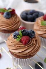 Tasty cupcakes with chocolate cream and berries on white table, closeup