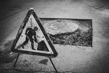 a close-up of a road repair sign against the backdrop of a broken highway with potholes and bumps...