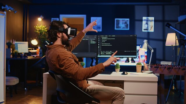 Remote software developer using VR goggles in personal office at home to do javascript programming. IT engineer wearing virtual reality headset in order to visualize lines of code, camera B