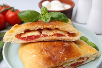 Pieces of tasty vegetarian calzone with tomato, cheese and basil on table, closeup
