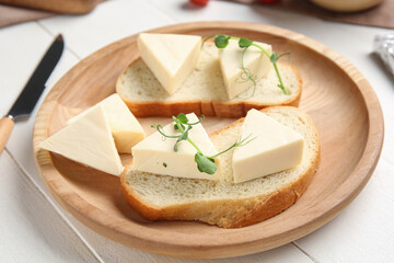 Plate with bread and triangles of tasty processed cheese on light wooden table, closeup