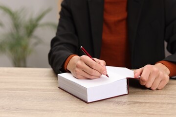 Writer signing autograph in book at wooden table indoors, closeup
