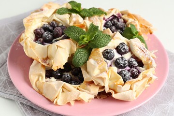 Tasty puff pastries with blueberries, powdered sugar and mint on table, closeup