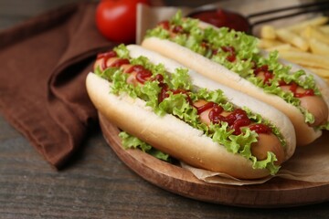 Tasty hot dogs with lettuce, ketchup and potato fries on wooden table, closeup
