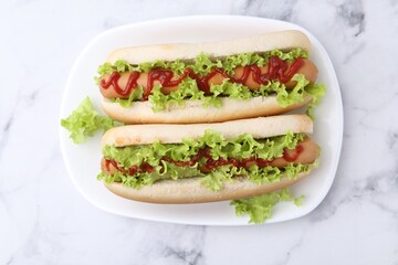 Tasty hot dogs with lettuce and ketchup on white marble table, top view