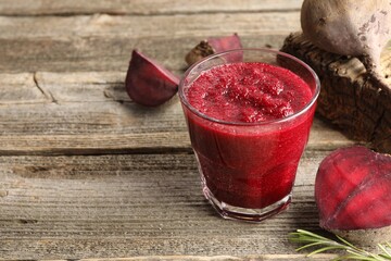 Fresh beetroot smoothie in glass, rosemary and cut vegetables on wooden table, closeup. Space for text