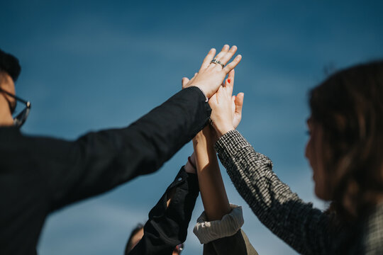 A dynamic image of business people coming together and celebrating success with a high five under the clear blue sky, symbolizing teamwork and unity.