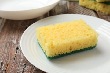 Yellow sponge, plate and bowl on wooden table, closeup
