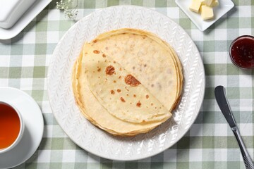 Delicious crepes, tea, butter and jam on table, flat lay