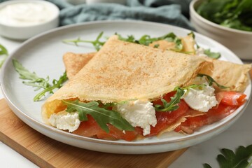 Delicious crepes with salmon, cream cheese and arugula on white table, closeup