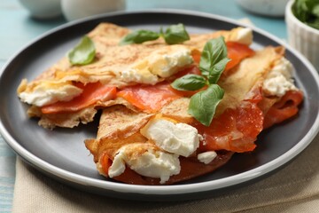 Delicious crepes with salmon, cream cheese and basil on table, closeup