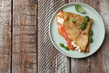 Delicious crepe with salmon, cream cheese and basil on wooden table, top view. Space for text