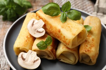 Delicious rolled crepes with mushrooms and basil on table, closeup