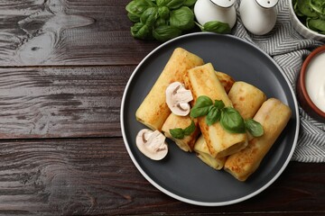 Delicious rolled crepes with mushrooms, basil and sour cream on wooden table, flat lay. Space for text