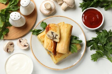 Delicious rolled crepes with mushrooms, parsley, sauce and sour cream on white marble table, flat lay