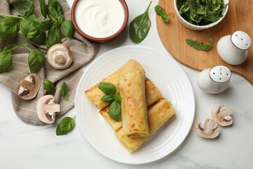 Delicious rolled crepes with mushrooms, basil and sour cream on white marble table, flat lay