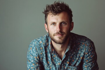 Obraz premium Portrait of a Stylish Young Man with a Beard in a Floral Shirt Against a Neutral Background
