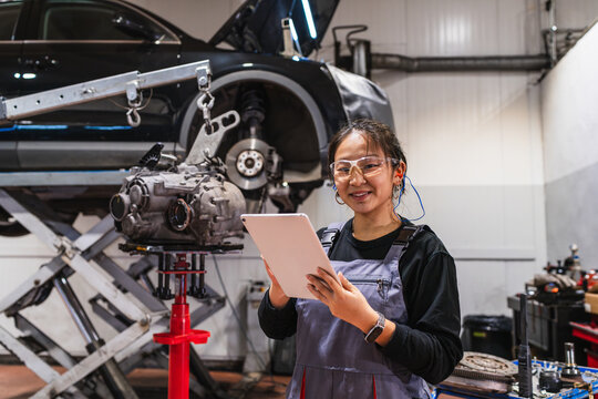 Young chinese female mechanic using digital tablet in auto repair shop - Powered by Adobe