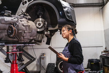 Female chinese mechanic inspecting car in auto repair shop