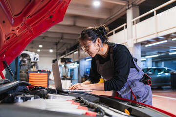 Female chinese mechanic using laptop while repairing car engine in garage