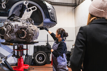 Female chinese mechanic installing gearbox in car repair shop with customer