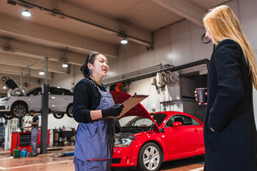 Female chinese mechanic explaining car repair to customer in auto shop