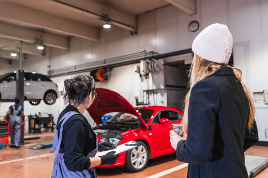 Female mechanic discussing car repair with customer in auto shop