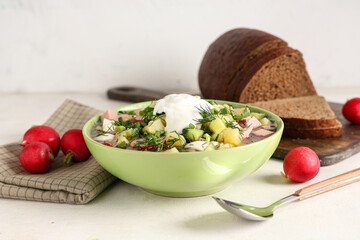 Bowl of tasty okroshka with sour cream, bread and fresh radish on light background