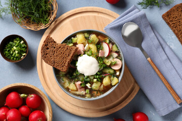 Composition with bowl of tasty okroshka, ingredients, bread and spoon on grey background