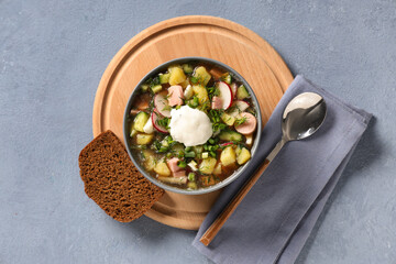 Bowl of tasty okroshka, bread and spoon on grey background