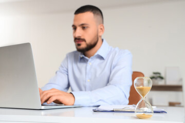 Hourglass on desk against businessman working with laptop in office, closeup