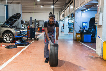 African mechanic lifting tire in auto repair shop