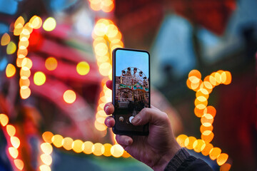 Hand with smartphone taking photos at the Christmas market, blurry bokeh lights in the background, copy space, selected focus