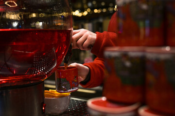 Hands of a woman in a red sweater tapping red mulled wine into a ceramic mug at the Christmas market, typical seasonal hot drink in Germany, copy space, selected focus