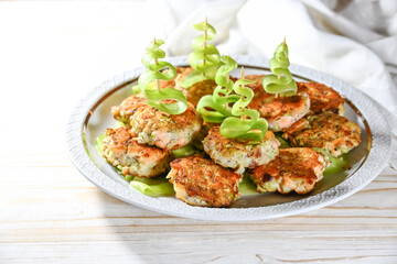 Small fried fish cakes or frikadelles with Christmas trees made of cucumber slices on a skewer, finger food for a festive holiday party on a white plate, copy space, selected focus